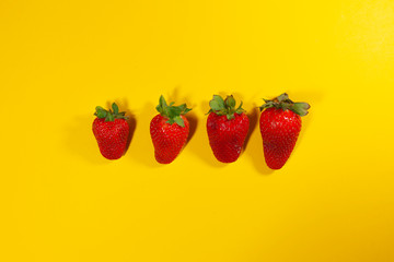 Four strawberries are laying in a row on a yellow surface