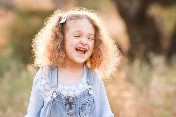 Laughing baby girl 3-4 year old having fun outdoors. Wearing stylish clothes. Summer time.