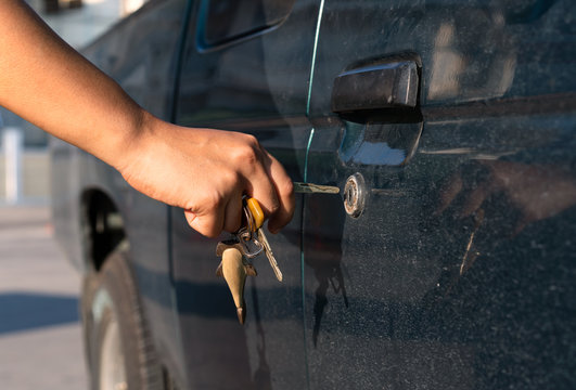 Side view of female hand in bright sunlight inserting a car key in to a door lock of a pickup truck - Tanned hand unlocking the door of an auto vehicle at sunset with metal keys