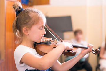 Child, little girl playing violin indoors in music class