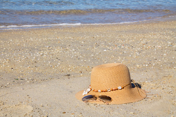 Hat and sunglasses. Beach accessories for sun protection on white sand, blue sky and sea background, summer holiday beach