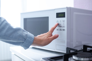 Woman warms up food in the microwave for lunch in the kitchen at home