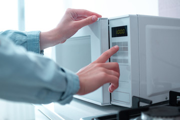 Woman warms up food in the microwave for lunch in the kitchen at home