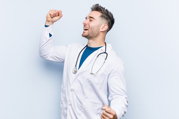 Young handsome doctor man raising fist after a victory, winner concept.