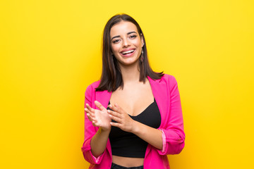 Young woman over isolated yellow background applauding after presentation in a conference