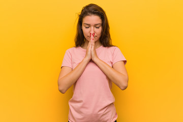 Young european woman isolated over yellow background holding hands in pray near mouth, feels confident.