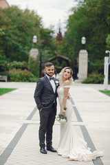 Fototapeta premium Beautiful bride in a long white dress. Handsome groom in a black suit. Couple in a summer park