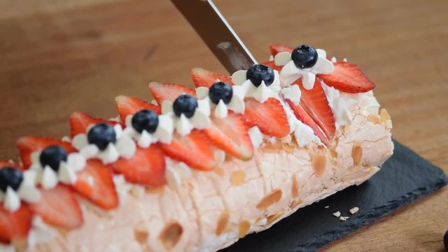 Close up, young girl is cutting meringue roulade with berries and mascarpone.