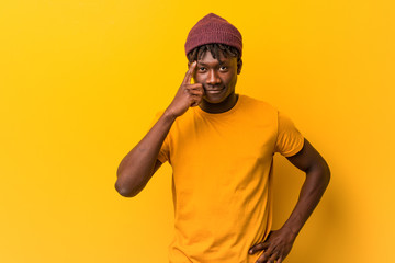 Young black man wearing rastas over yellow background pointing temple with finger, thinking,...