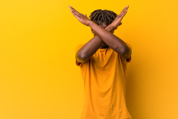 Young black man wearing rastas over yellow background keeping two arms crossed, denial concept.