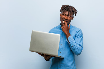 Young rasta black man holding a laptop relaxed thinking about something looking at a copy space.