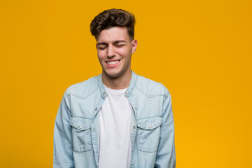 Young handsome student wearing a denim shirt laughs and closes eyes, feels relaxed and happy.