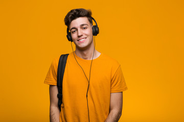 Young cool student man listening to music with headphones smiling and raising thumb up