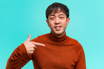 Young chinese man person pointing by hand to a shirt copy space, proud and confident