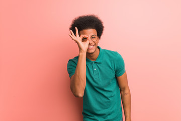 Young african american man over a pink wall confident doing ok gesture on eye