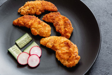 Fried chicken sirloin in breadcrumbs on a black dish.
