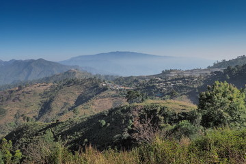 Fototapeta na wymiar Mountain view misty morning of Nor Lae Hill Tribes Village on top hill around with many mountains, green forest and blue sky background, Doi Ang Khang, Chiang Mai, Thailand.