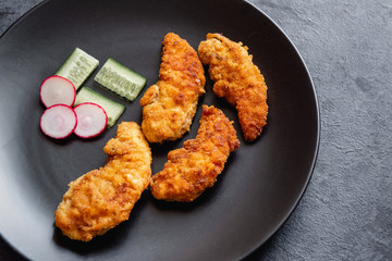 Fried chicken sirloin in breadcrumbs on a black dish.