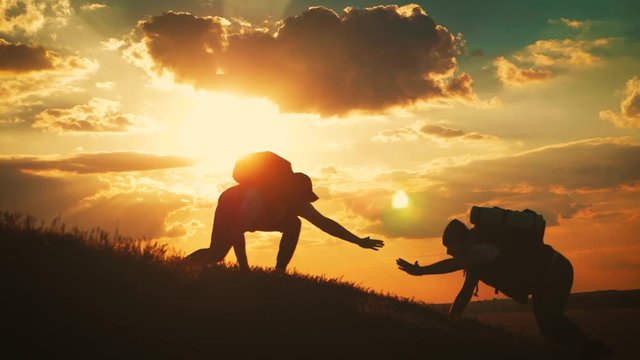 Silhouette of helping hand between two climber. two hikers on top of the mountain, a man helps a man to climb a sheer stone. couple hiking help each other silhouette in mountains with sunlight.