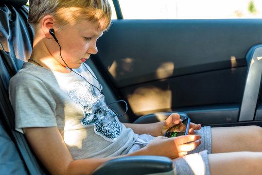 child with earphones inside car watching movie or listening music on his smartphone
