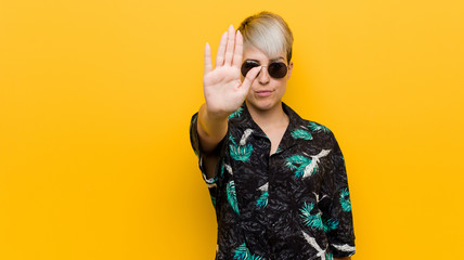 Young curvy woman wearing a summer look standing with outstretched hand showing stop sign, preventing you.
