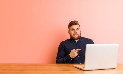 Young man working with his laptop shocked pointing with index fingers to a copy space.