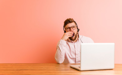 Young man working in a call center yawning showing a tired gesture covering mouth with him hand.