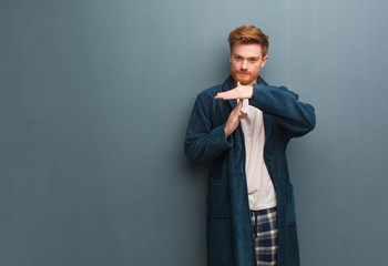 Young redhead man in pajama doing a timeout gesture