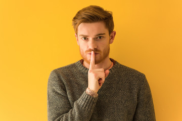 Young redhead man face closeup keeping a secret or asking for silence