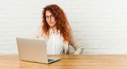 Young redhead curly woman working with her laptop confident keeping hands on hips.