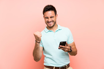 Handsome young man over isolated background with phone in victory position