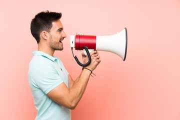 Handsome young man over isolated background shouting through a megaphone