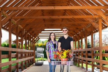 Young couple with a carriage full of different plants in the greenhouse