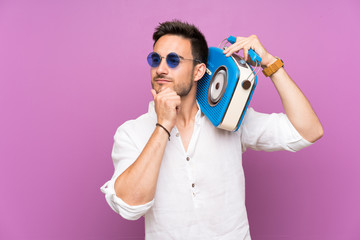 Handsome young man over purple background holding a radio