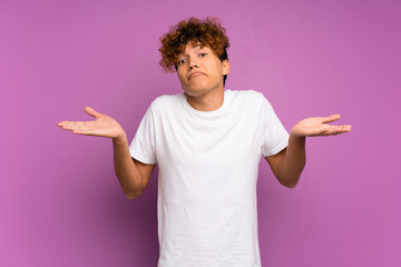 Young african american man over isolated purple wall having doubts while raising hands