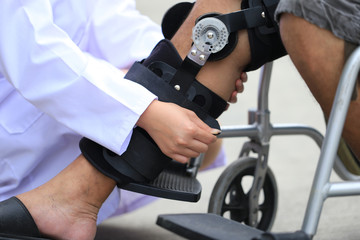 Physiotherapist fixing knee braces of senior man leg with sitting on the wheelchair, Medical and healthcare concept