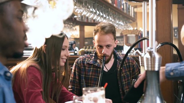 Five multi ethnic friends relaxing with shisha or hookah in bar.