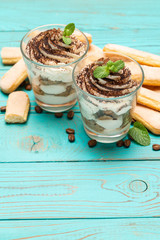 Classic tiramisu dessert in a glass and savoiardi cookies on blue wooden background