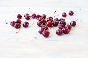 A lot of red berries of sweet cherry scattered on light wooden table close up, bunch of ripe cherry...