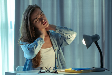 Tired overworked woman feeling fatigue, neck pain and massaging neck while working late at night at...