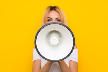 Young blonde woman over isolated yellow wall shouting through a megaphone