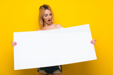 Young blonde woman over isolated yellow wall holding an empty white placard for insert a concept