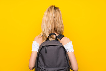 Young blonde woman over isolated yellow wall with backpack