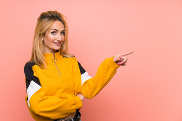 Young blonde woman over isolated pink background pointing finger to the side
