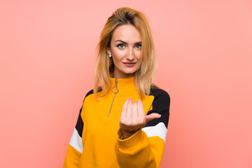 Young blonde woman over isolated pink background inviting to come with hand. Happy that you came