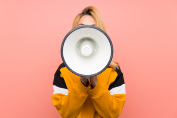Young blonde woman over isolated pink background shouting through a megaphone
