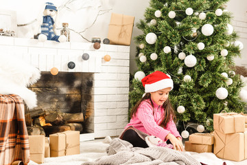 Happy little girl with Christmas present laying by the fire in front of xmas tree