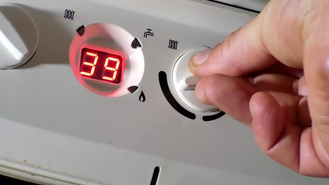 Male hand turning boiler temperature knob down to save money & conserve energy. Push in closeup.