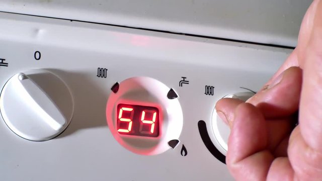 Male hand turning boiler temperature knob up to make room warm & comfortable. Pull back from closeup.