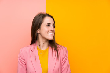 Fototapeta premium Young woman with pink suit over colorful background laughing and looking up